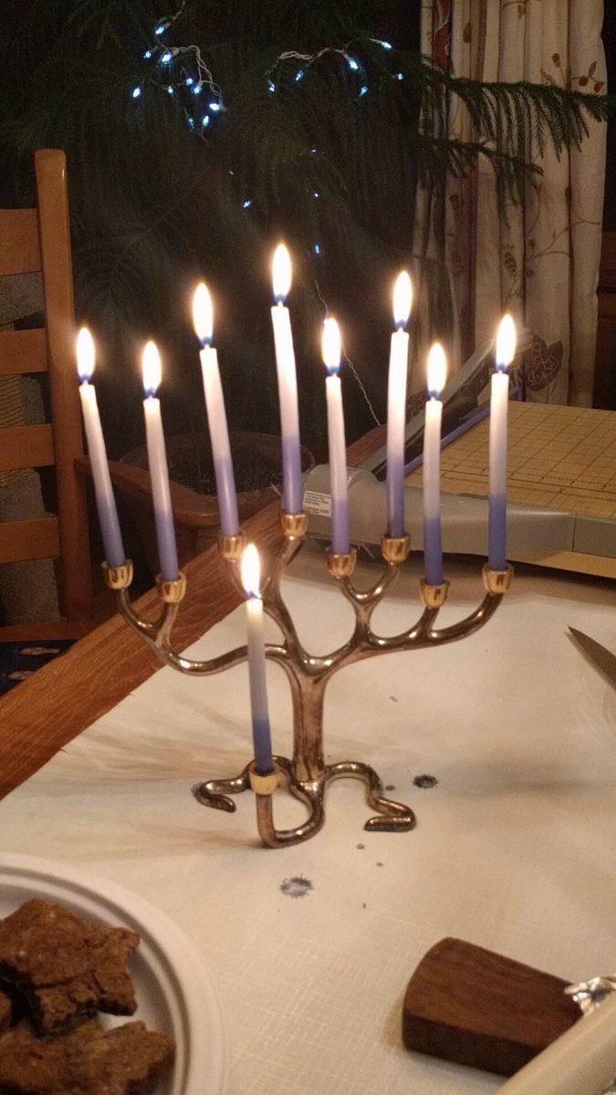 A menorah sits glowing on a table. Menorahs are lit during the eight days of Hanukkah, symbolizing Jewish resilience. Photo by Camilla Baudhuin