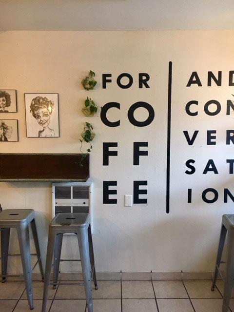 One of the interior walls of Peaks Coffee PDX displays the coffee shop’s cheerful motto: “For coffee and conversation.” Photo by Abby Watters.