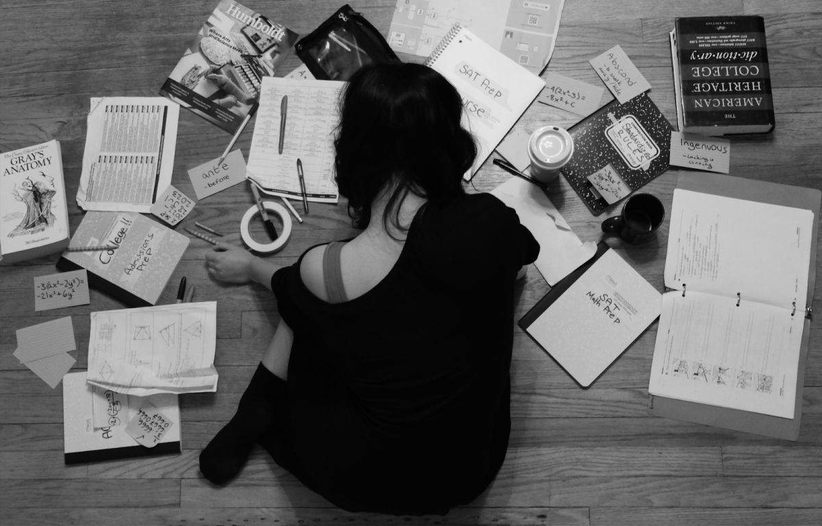 Student dressed in black crumpled on the floor, surrounded by strewn-about papers, flashcards, notebooks, and other school supplies for SAT preparation. The SAT can create unnecessary stress and overwhelm even the best of students. Photo by