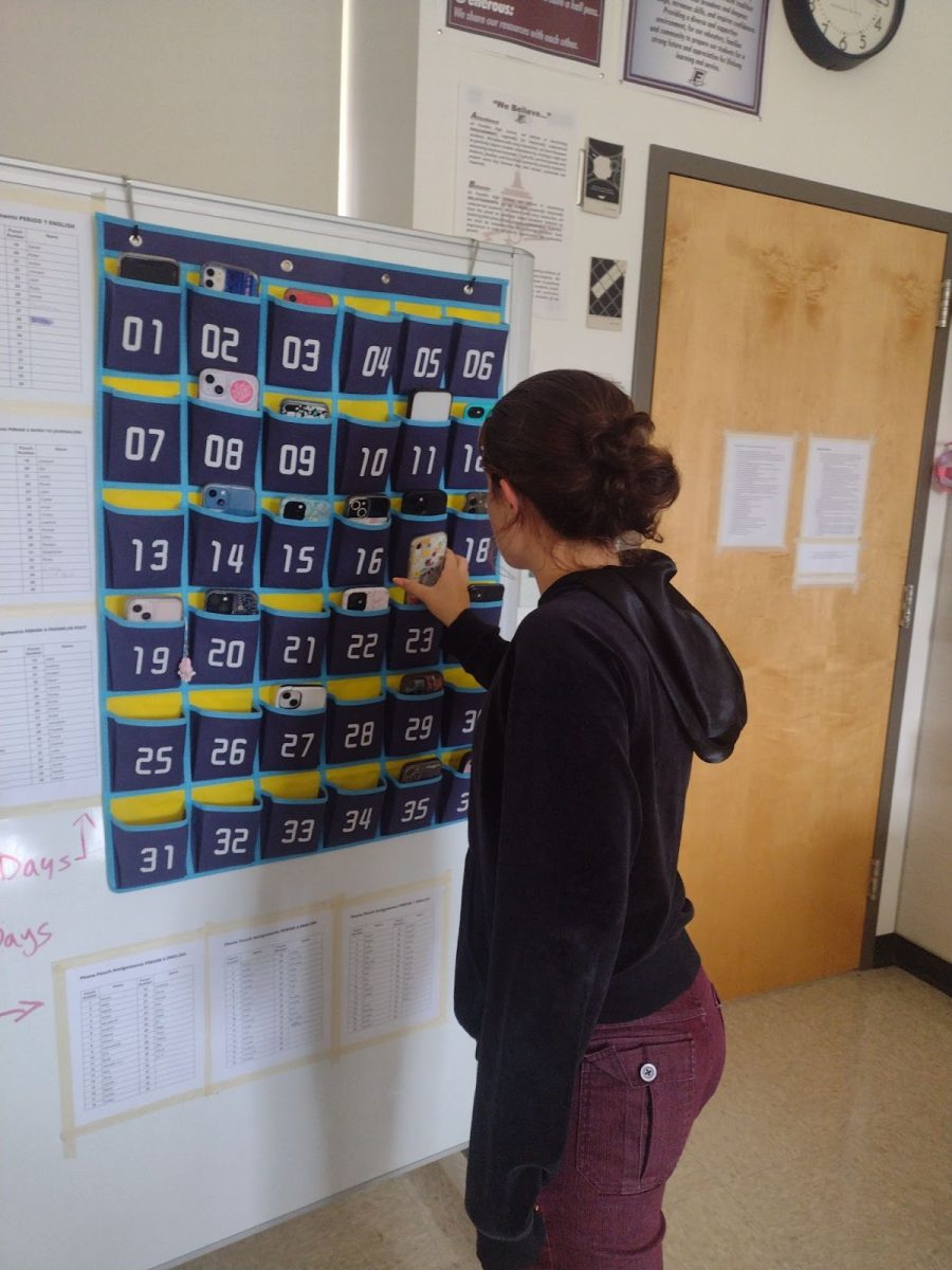 A student places her phone into a mostly-full pocketed phone holder, now standard in Franklin classrooms. The newly instituted policy at Franklin requires phones to be placed in these holders for the duration of class.