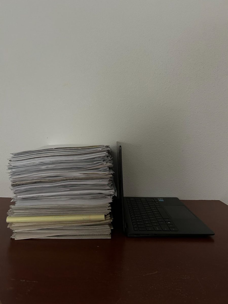 A stack of paper directly next to a computer. The ongoing battle between doing things on paper versus digitally is extremely controversial in education, especially when it comes to testing. Photo by 