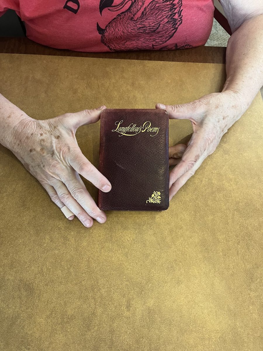 Hands displaying a poetry book that has been passed down through generations. This book is among the many things that Helen Kelley chose to keep as she has aged, just like each person is tasked with the responsibility of choosing what items they will preserve. Photo by 