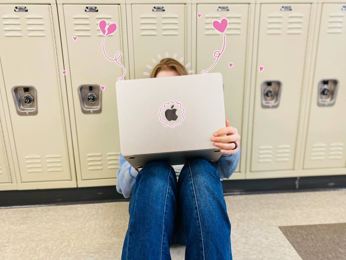 A teenager sitting against school lockers, absorbed in her computer, from which hearts spiral. It is very common for adolescents in fandoms to spend excessive amounts of time online becoming emotionally attached to fictional characters and worlds. Photo by Easton Atlansky.