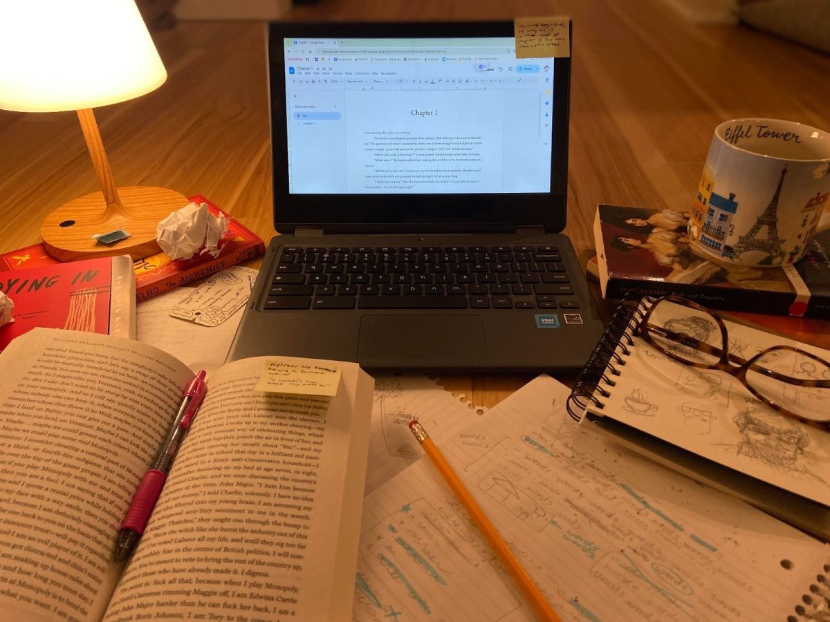 Journals, books, and scraps of paper are scattered around an open computer displaying a document titled “Chapter 1.” Many teens have an interest in writing, but it can be challenging to get started with limited experience or support. Photo by Margot Atchison.