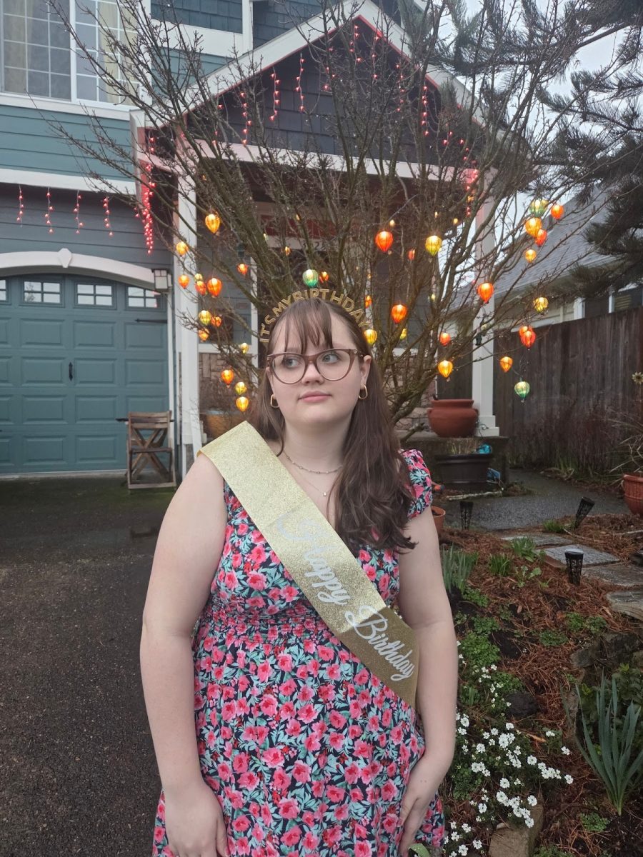 A girl decked in a birthday headband and sash stands in front of a house decorated for Christmas. What happens when holidays and birthdays share a date? Photo by Fiona Snyder.