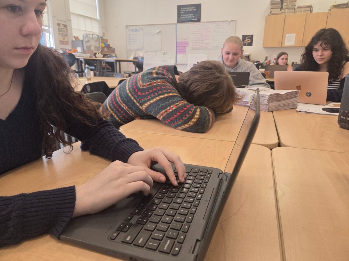 A student sleeps at their desk while classmates work around them. Getting enough sleep is a significant issue for high school students, and a struggle that could be relieved by having designated resting or nap time. Photo by 